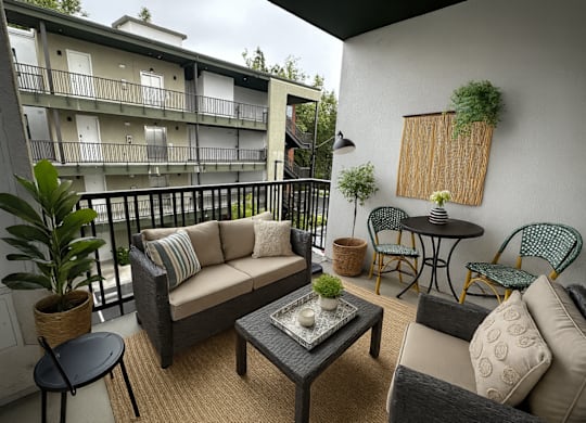 A balcony with a couch, chairs, and a table with a potted plant on it.