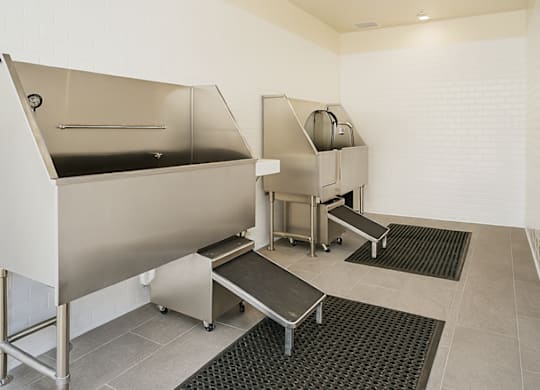 A clean, empty industrial kitchen with stainless steel appliances and black mats on the floor.
