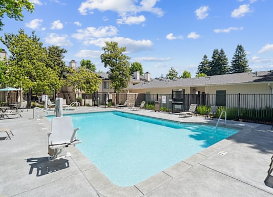 A large swimming pool surrounded by lounge chairs and trees.