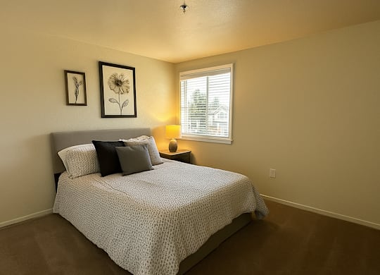 A bedroom with a bed, pillows, a lamp, and pictures on the wall.