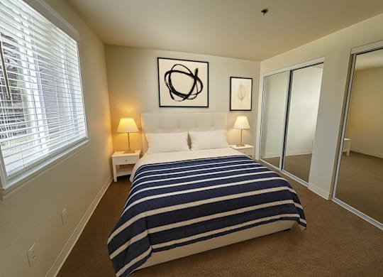 A bedroom with a bed, two lamps, and a mirror.