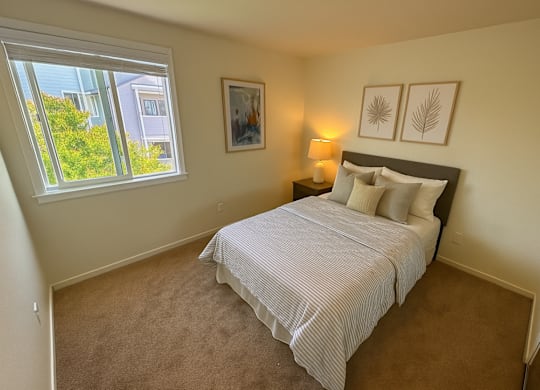 A bedroom with a bed, two pictures on the wall, and a window with a view of a building outside.