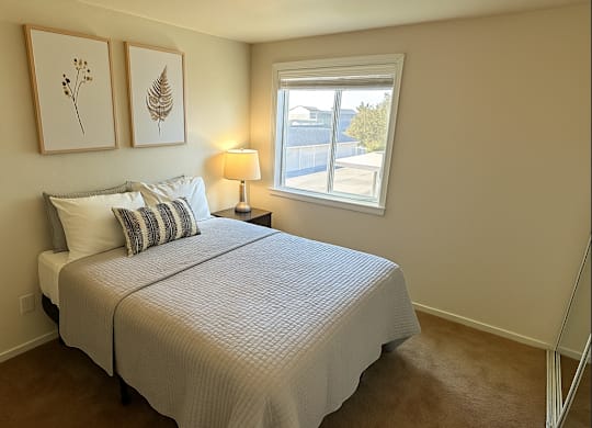 A bedroom with a bed, pillows, a lamp, and two framed pictures on the wall.