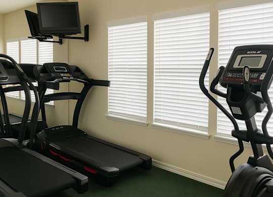 A gym with treadmills, elliptical machines, and a television.