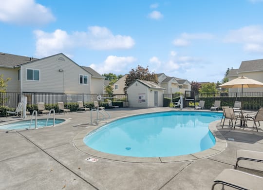 A swimming pool surrounded by lounge chairs and umbrellas in a residential area.