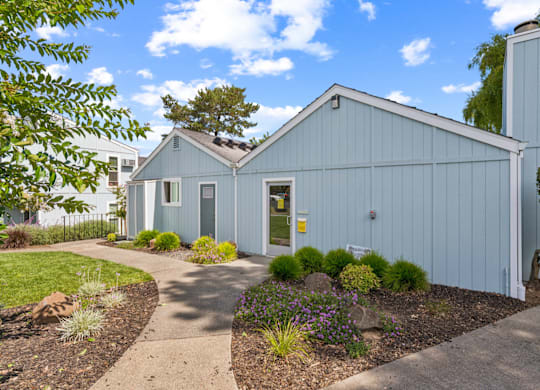 A blue building with a white door and windows is surrounded by a garden.