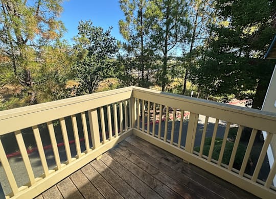 A wooden deck with a railing and a view of trees and a house.