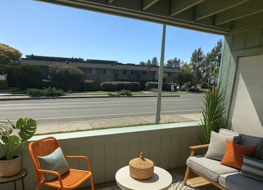 A patio with a chair, a table, and a couch with a view of the street.