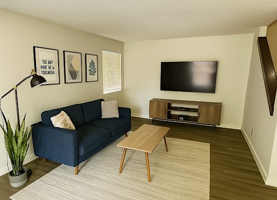 A living room with a blue couch, a wooden coffee table, and a flat screen TV mounted on the wall.