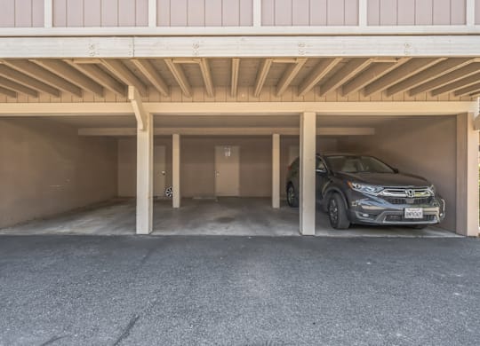 A car is parked in a garage under a wooden beam.