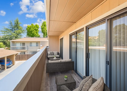 A balcony with a couch and a table with a glass door.