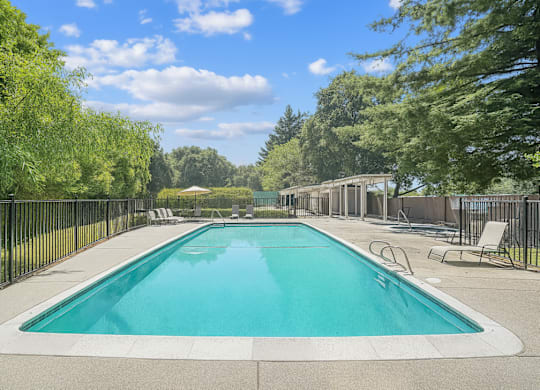 A large outdoor swimming pool surrounded by trees and a fence.