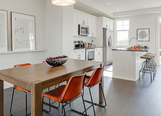 A modern kitchen with a wooden dining table and orange chairs.