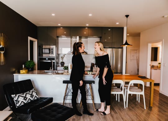two women standing in a living room in a kitchen