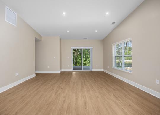 A spacious room with wooden flooring and a sliding glass door leading to a balcony.