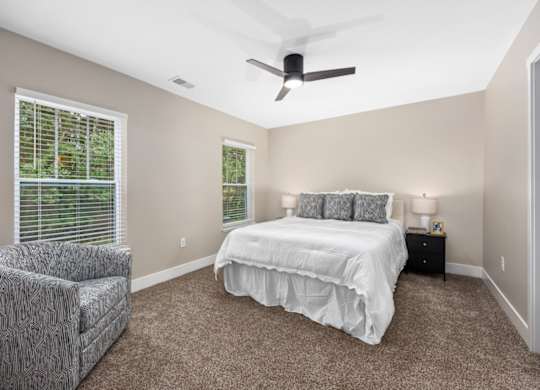 A bedroom with a bed, chair, and ceiling fan.