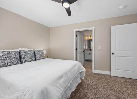 A bedroom with a white bed and a ceiling fan.