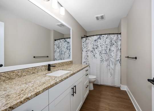 A bathroom with a marble countertop and a floral shower curtain.