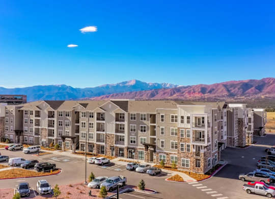 A large apartment complex with a parking lot in front and mountains in the background.