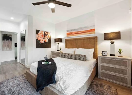 A bedroom with a large bed, a ceiling fan, and a painting on the wall.