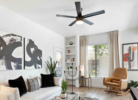 A living room with a white couch, a glass coffee table, a rocking chair, and a ceiling fan.