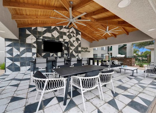 A patio with a table and chairs under a wooden roof.
