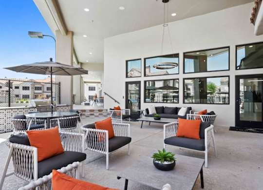 A patio with white chairs and orange cushions.