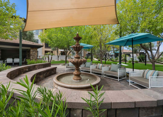 a fountain in the middle of a patio with chairs and umbrellas