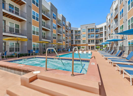 a pool with lounge chairs and umbrellas in front of an apartment building