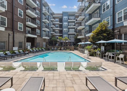 an outdoor swimming pool with lounge chairs and umbrellas in front of an apartment building