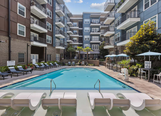 an outdoor swimming pool with lounge chairs and umbrellas in front of an apartment building