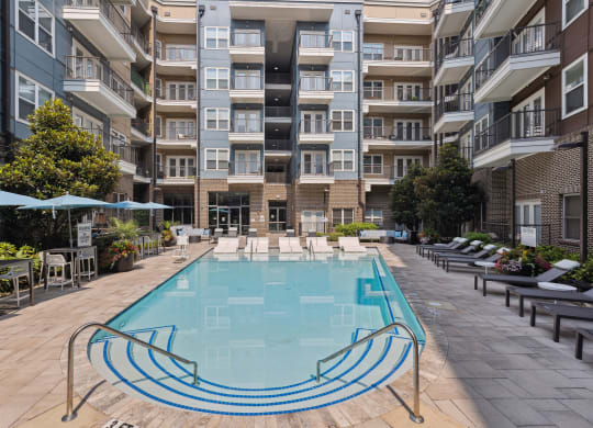 an outdoor swimming pool with lounge chairs and umbrellas in front of an apartment building
