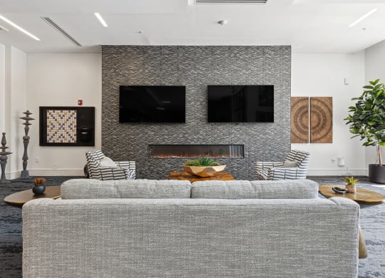 a living room with a gray couch and two televisions on the wall