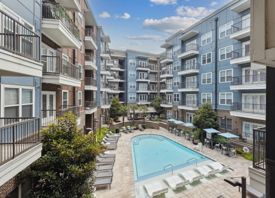 an outdoor pool with lounge chairs and umbrellas in front of an apartment building