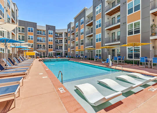 A swimming pool surrounded by sun loungers and apartment buildings.