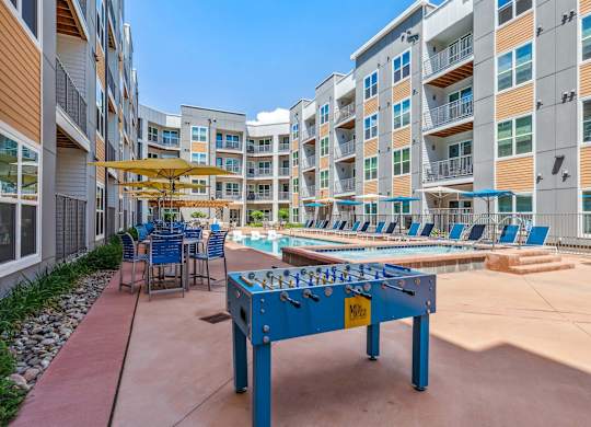 A blue foosball table is in the middle of a courtyard with chairs and umbrellas.