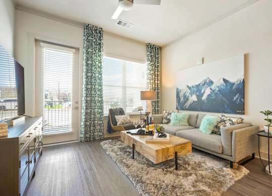 A living room with a grey couch and a large mountain painting on the wall.