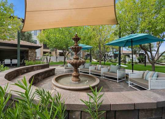 A fountain in the middle of a patio with a shade sail over it.