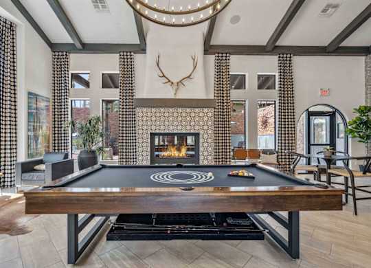 A pool table is in the middle of a room with a fireplace and a deer head mounted on the wall.