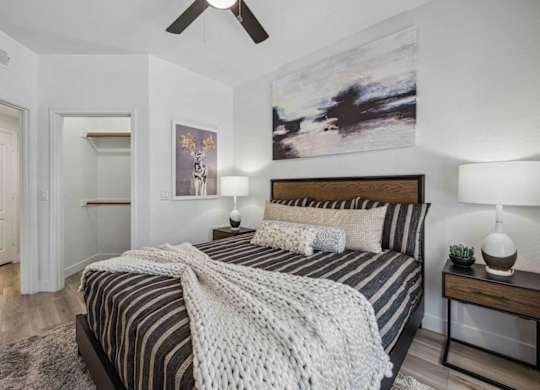 A bedroom with a bed, two lamps, and a painting on the wall.