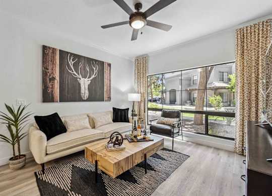 A living room with a white couch, a wooden coffee table, and a deer head picture on the wall.