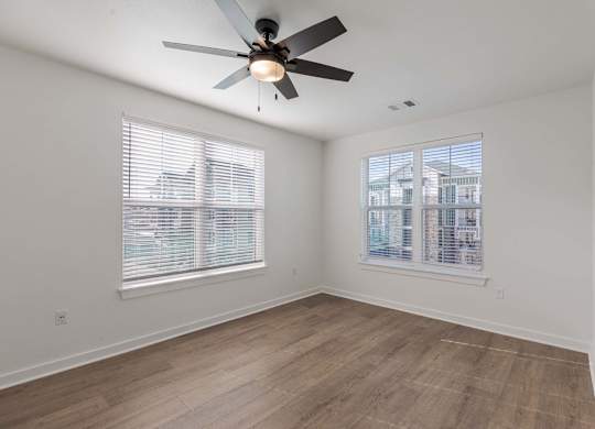 A room with a ceiling fan and two windows.