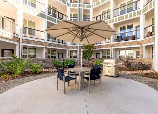 A patio with a table and chairs and an umbrella in front of apartment buildings.