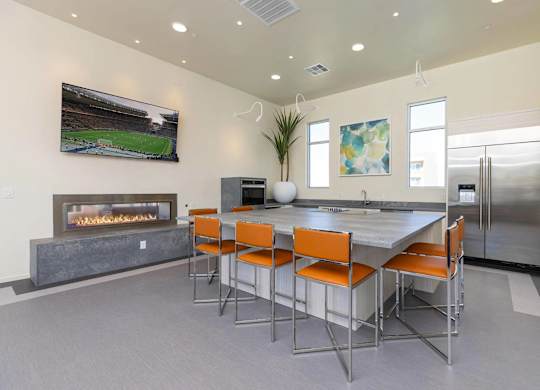 A modern kitchen with a fireplace and a dining table with orange chairs.