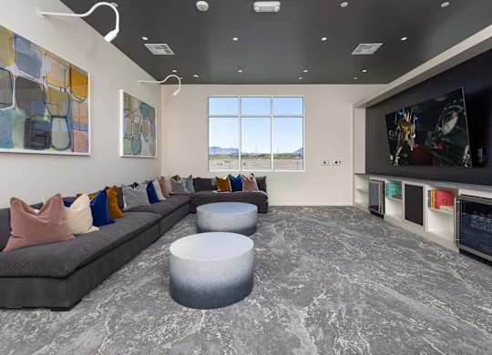 A modern living room with a grey sofa, a grey ottoman, and a large flat screen TV mounted on the wall.