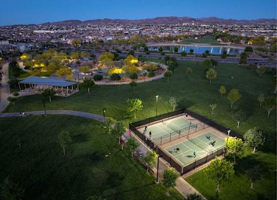 Tennis court surrounded by green grass and trees with people playing.