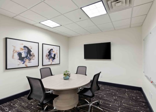 a meeting room with a round table and chairs and a flat screen tv on the wall