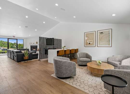 A spacious living room with grey armchairs, a wooden coffee table, and a large window with blinds.