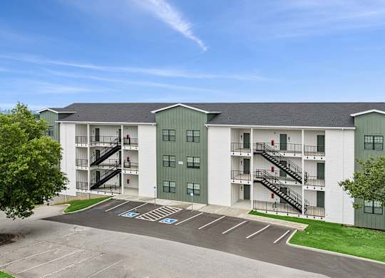 A large white and green apartment complex with a parking lot in front.