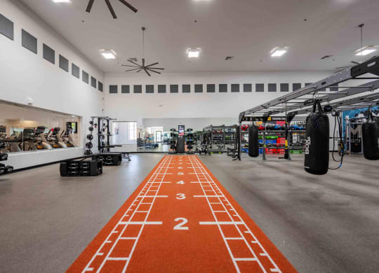 a spacious fitness center with a red track running down the middle of the room and weights on